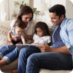 Family sits together on a couch reading a children’s book.